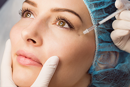 A needle is inserted into a woman's face for a cosmetic procedure.
